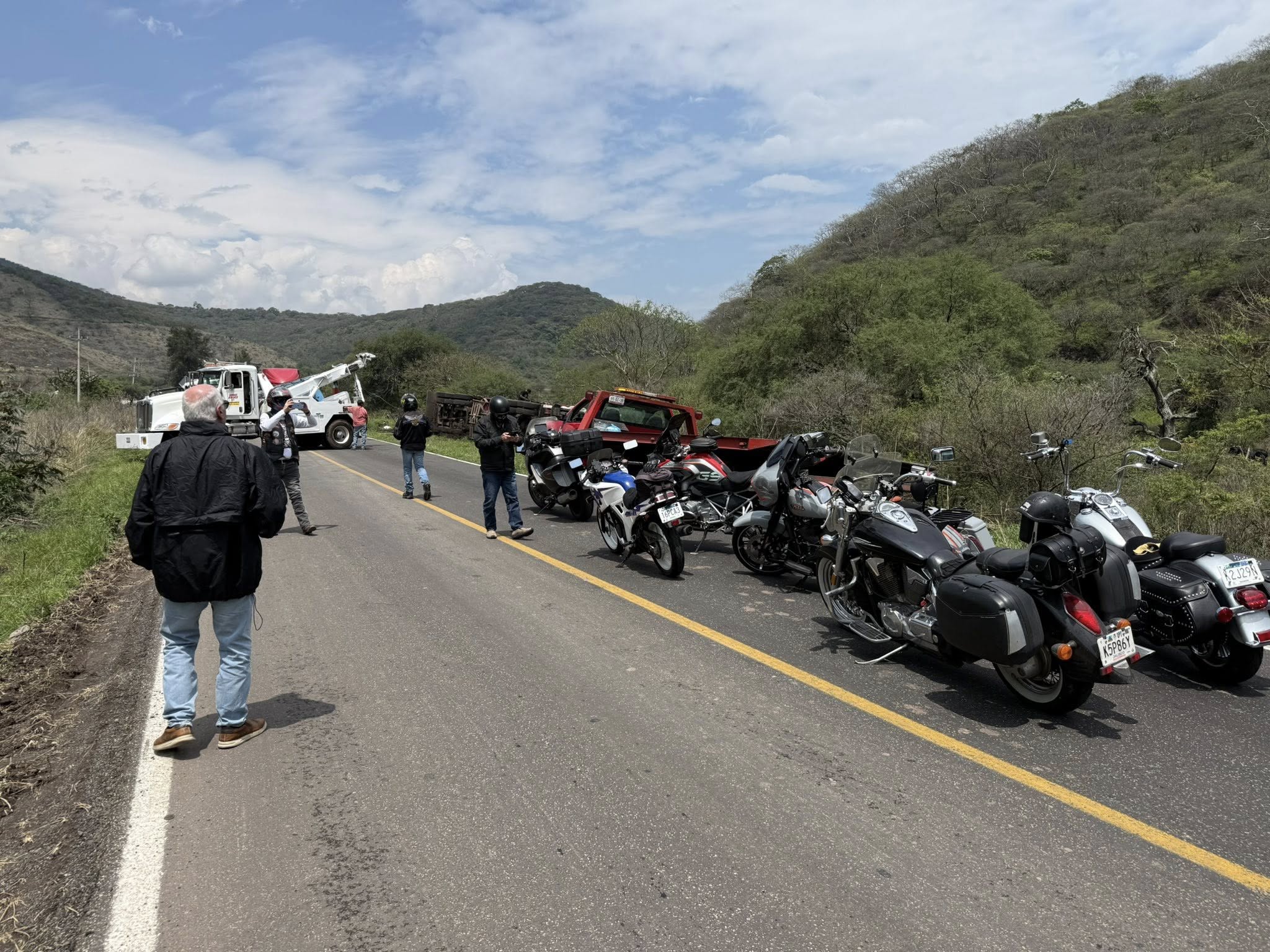 Club motorcycles pulled over on a mountain road while a tow truck clears an overturned truck